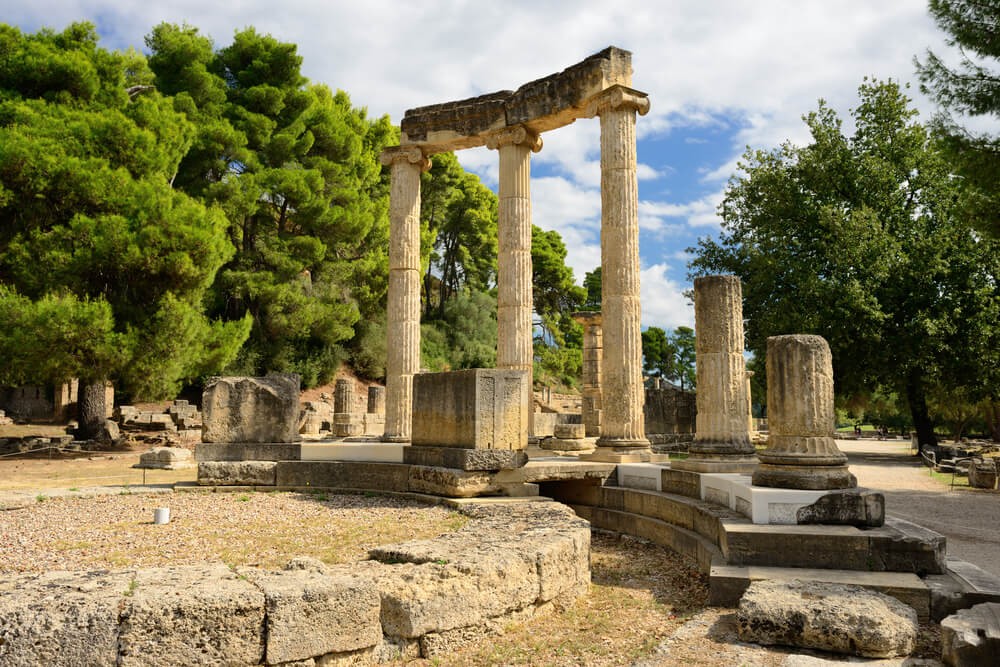 Peloponnese peninsula: Old columns in a circle surrounded by trees in Olympia