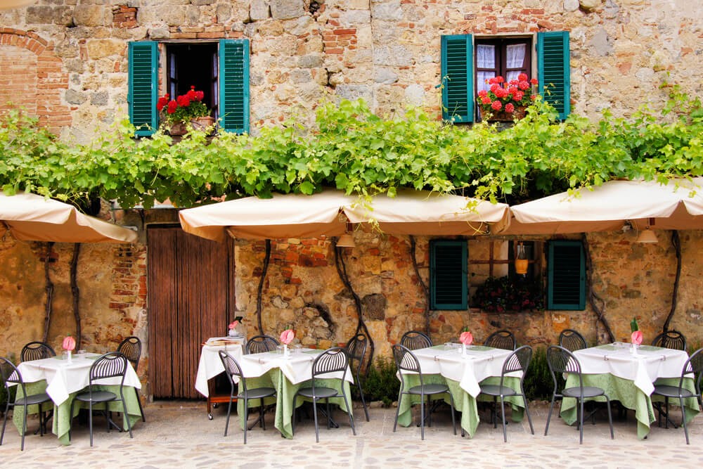 Traditional trattoria: A stone brick restaurant in Rome with four green tables outside