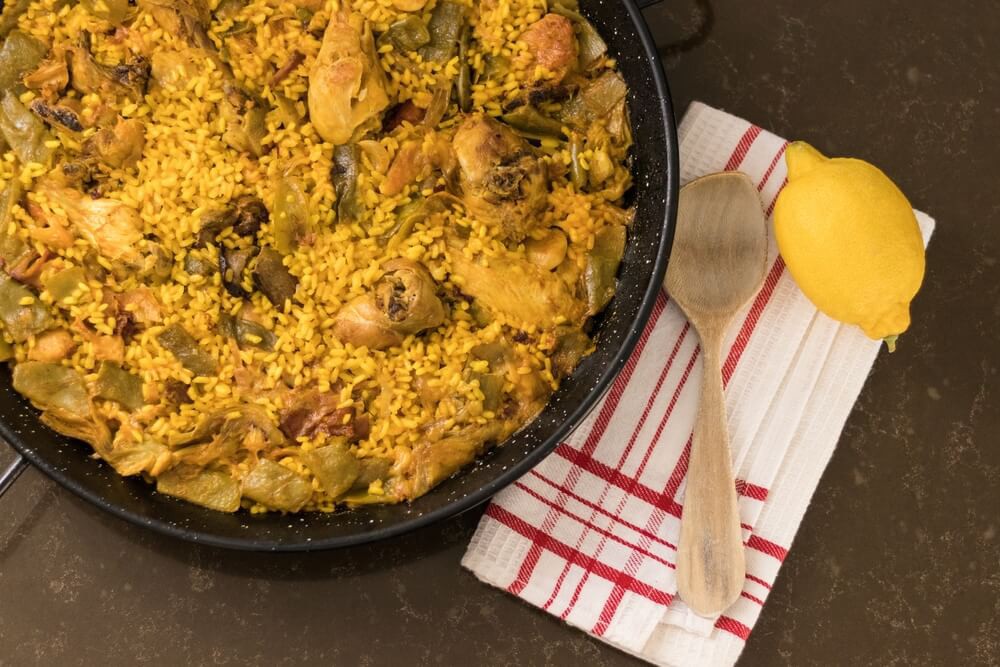 Origins of paella: A paella pan full of Valencian paella with a wooden spoon and lemon