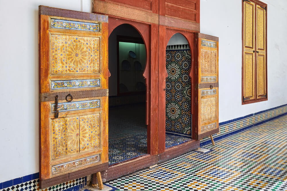 Dar Batha: A white wall with big wooden doors painted in an ornate style