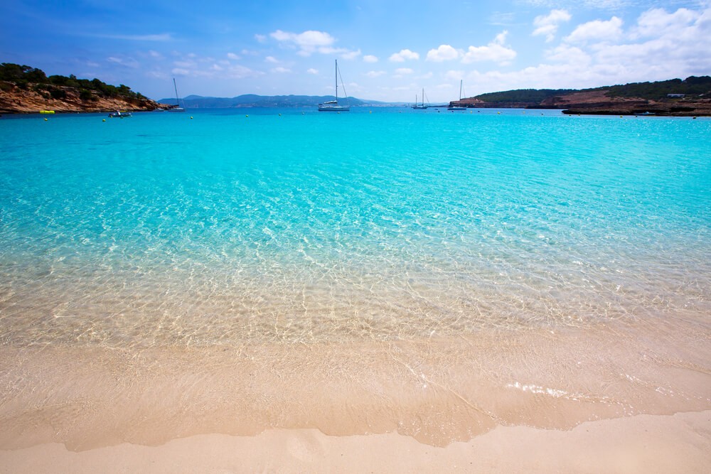 Cala Bassa: Large open bay with golden sand and clear sea and 4 sailing boats in the distance