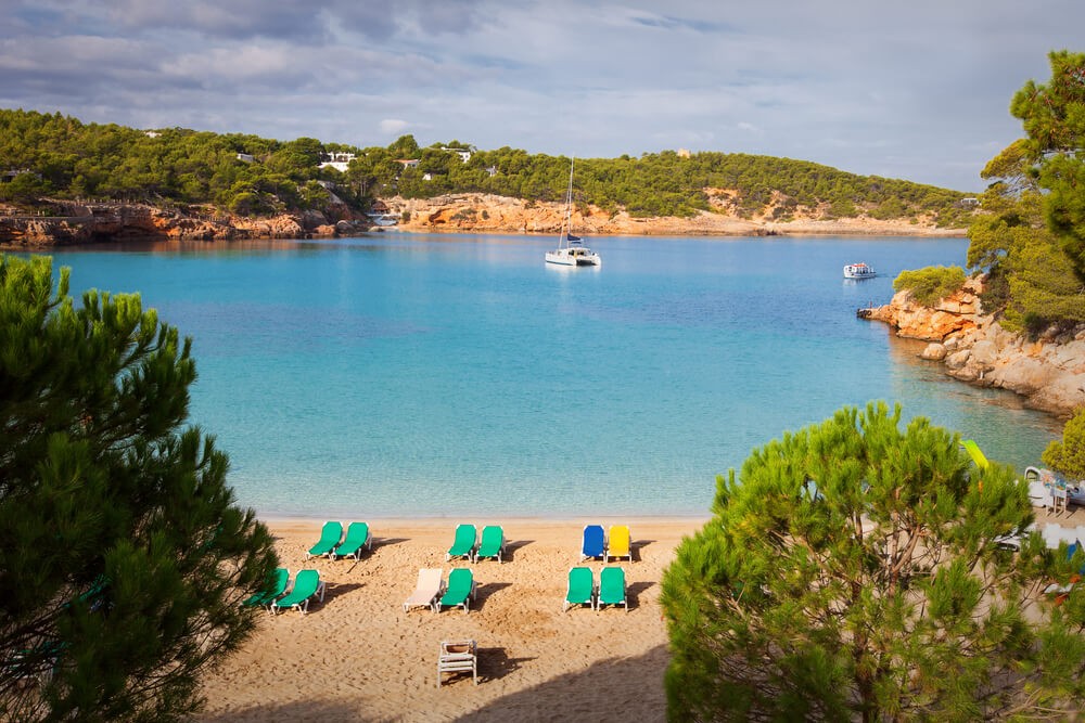 Best beaches in Ibiza: Golden sand beach dotted with loungers surrounded by greenery