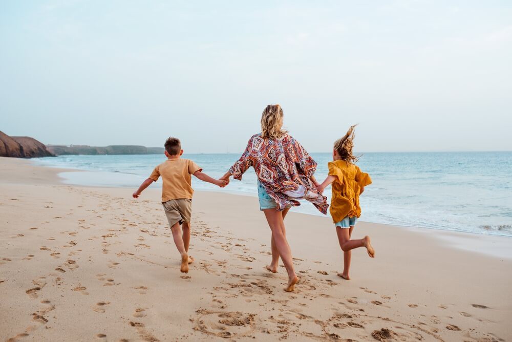 Family holidays in Lanzarote: A blonde haired woman walking hand in hand on the beach with two kids