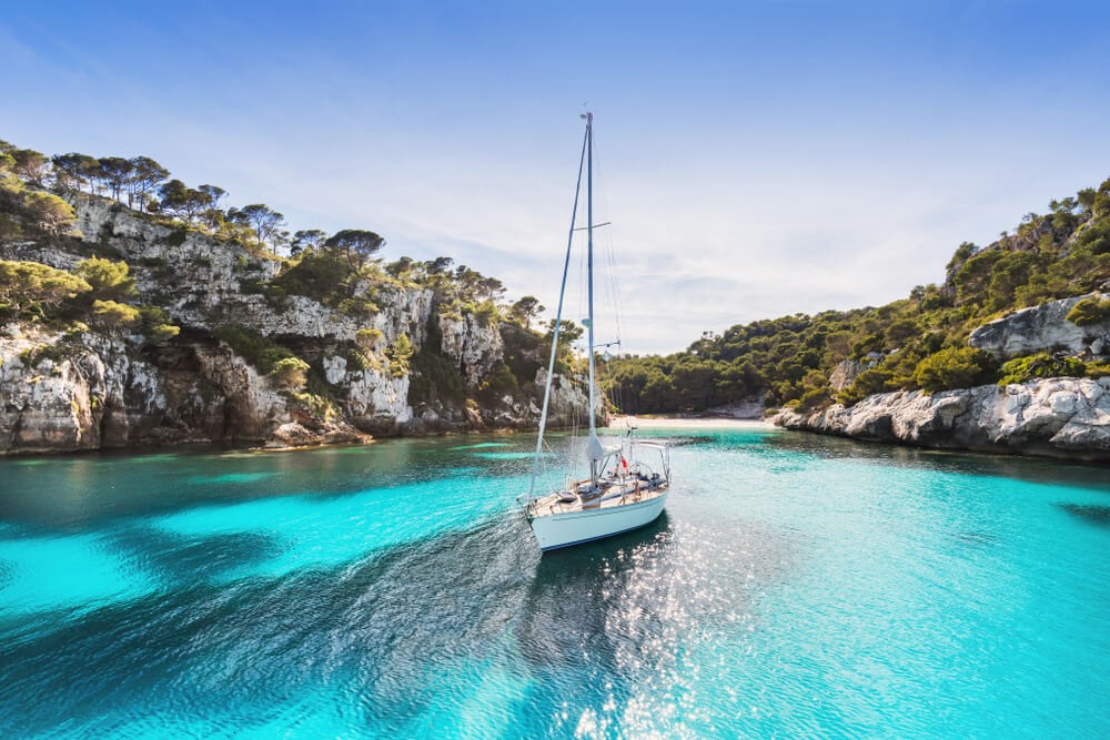 Watersports in Mallorca: Sailing boat on topaz waters in a cove with rocky surroundings