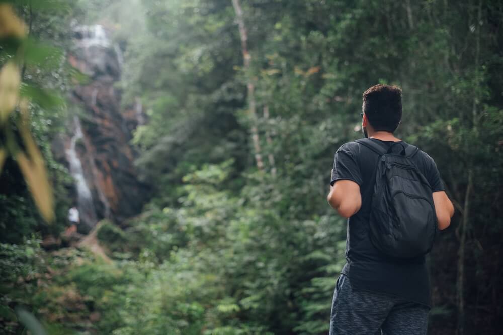 A man hiking in a tropical forest with a waterfall in the background. 