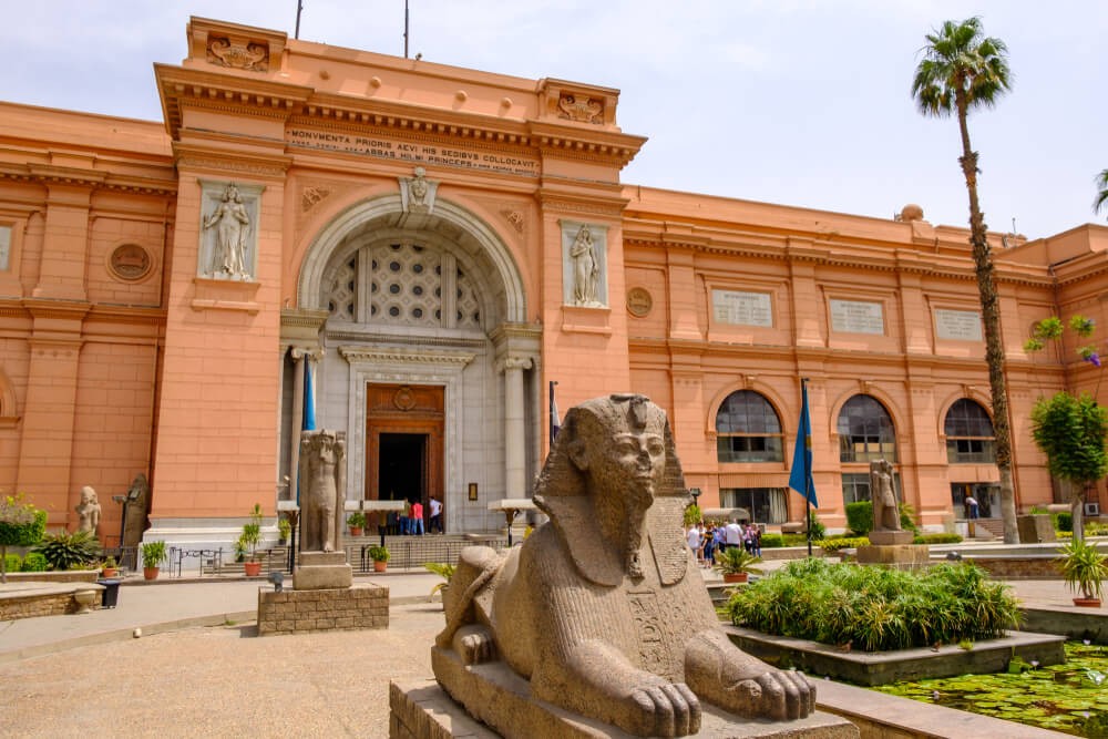 Things to do in Cairo: Red brick facade of the Egyptian Museum with a Sphinx outside