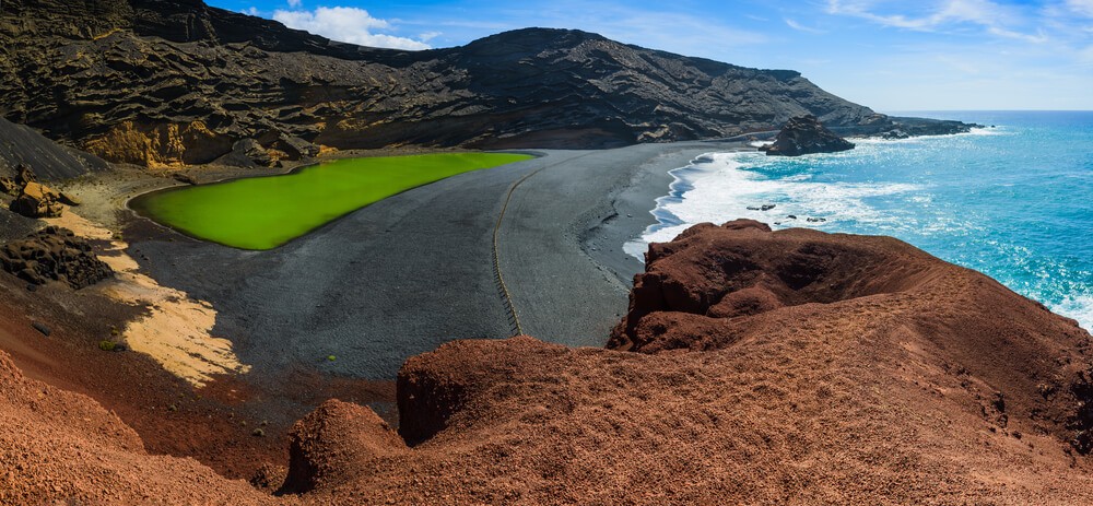 Things to do in Lanzarote: Black sand and mountains surrounding a green 