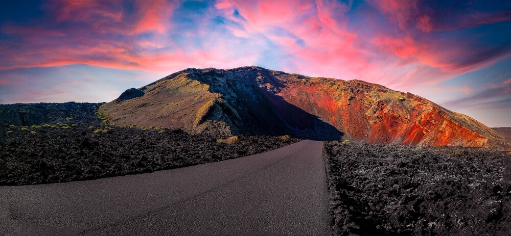 Timanfaya National Park: The sun setting over a black sand road and volcano